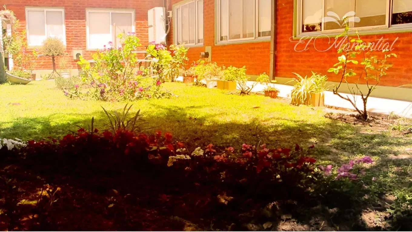 Un exuberante jardín verde con flores vibrantes en primer plano, con un edificio de ladrillo rojo 
