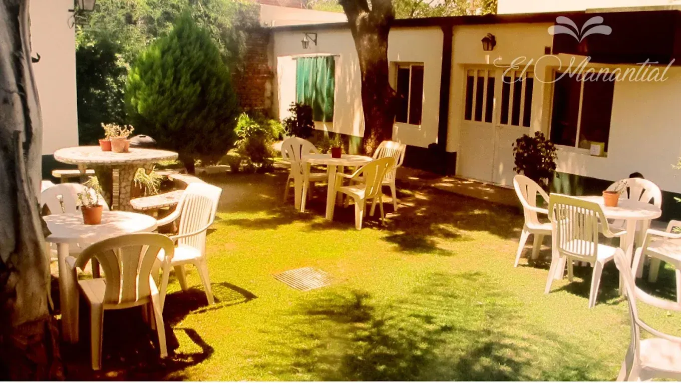 Zona de comedor al aire libre con mesas y sillas de plástico blanco, situada en un patio cubierto de césped 