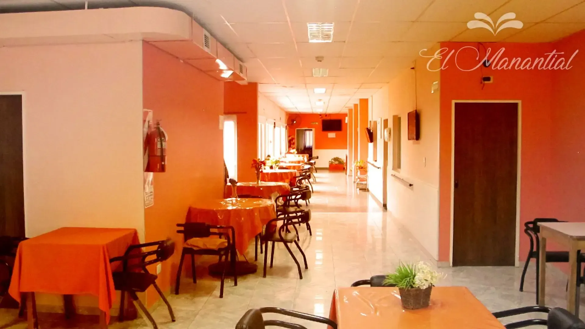 Un comedor luminoso con paredes naranjas, varias mesas cubiertas con manteles naranjas y sillas 