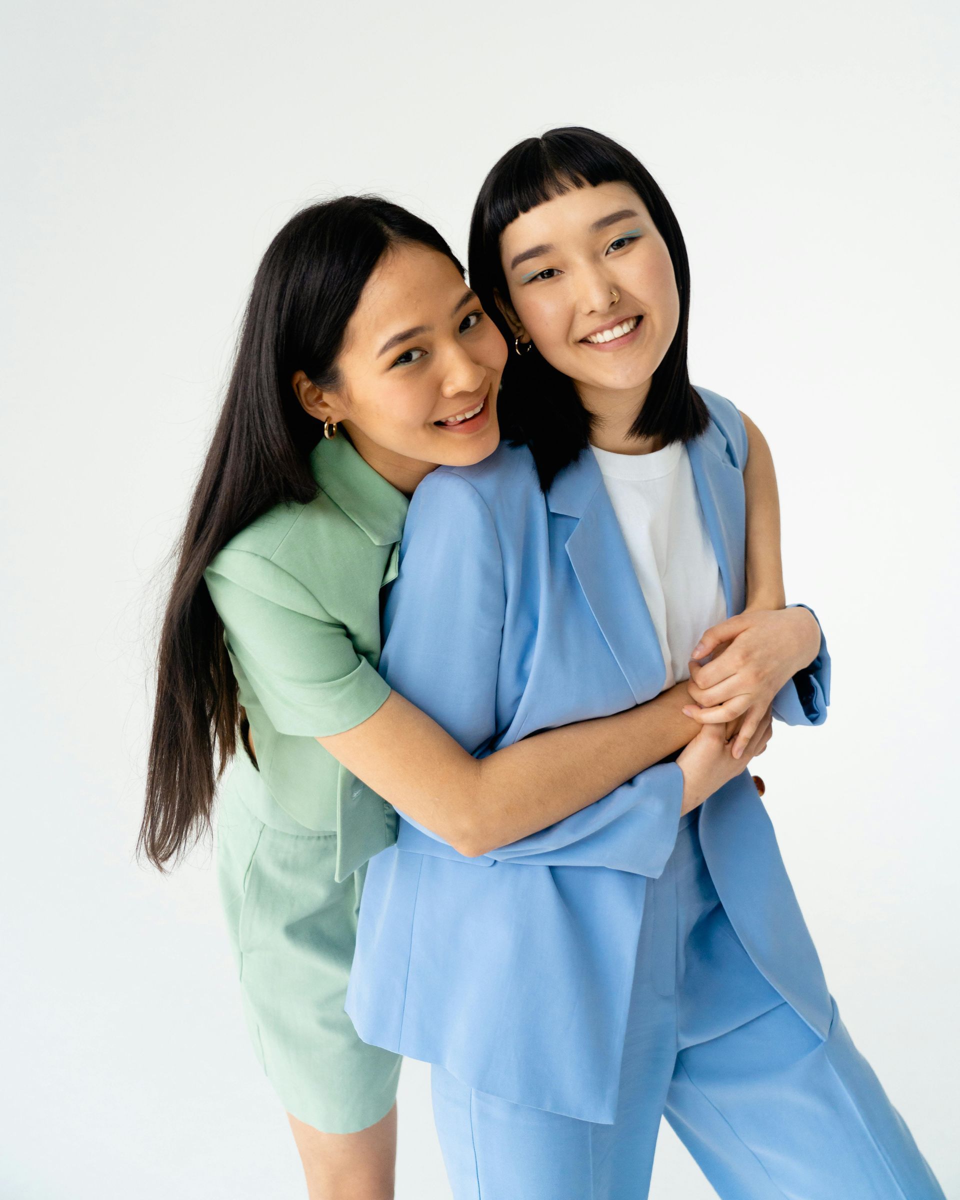 Two women in suits are hugging each other on a white background.