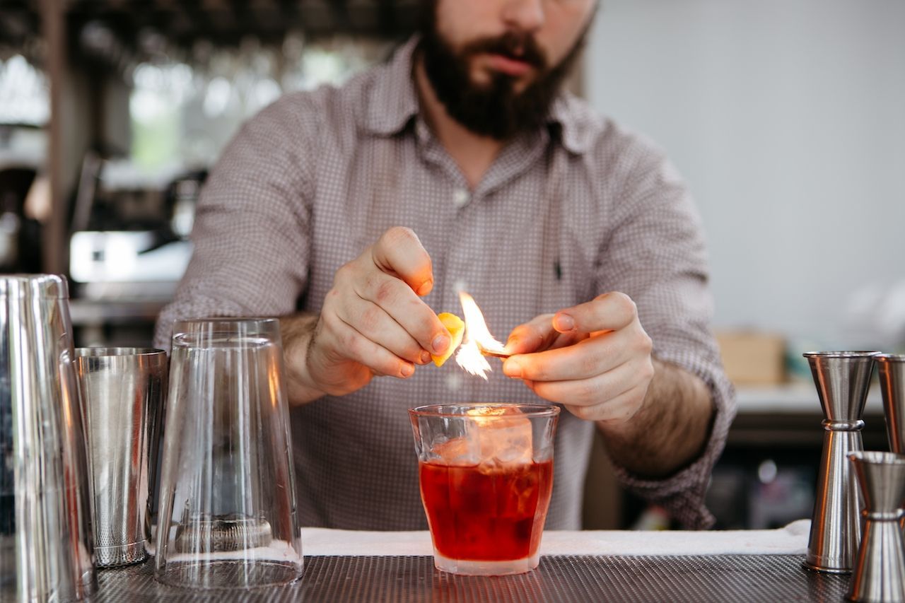 A bartender is lighting an orange peel to make a drink.