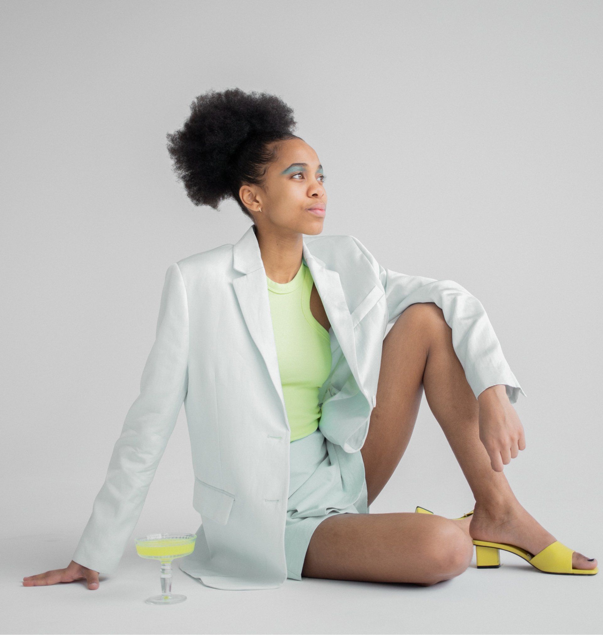 A woman in a white jacket and shorts is sitting on the floor with her legs crossed.