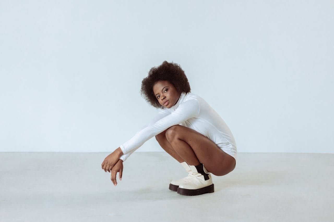 A woman in a white bodysuit is squatting on the floor.