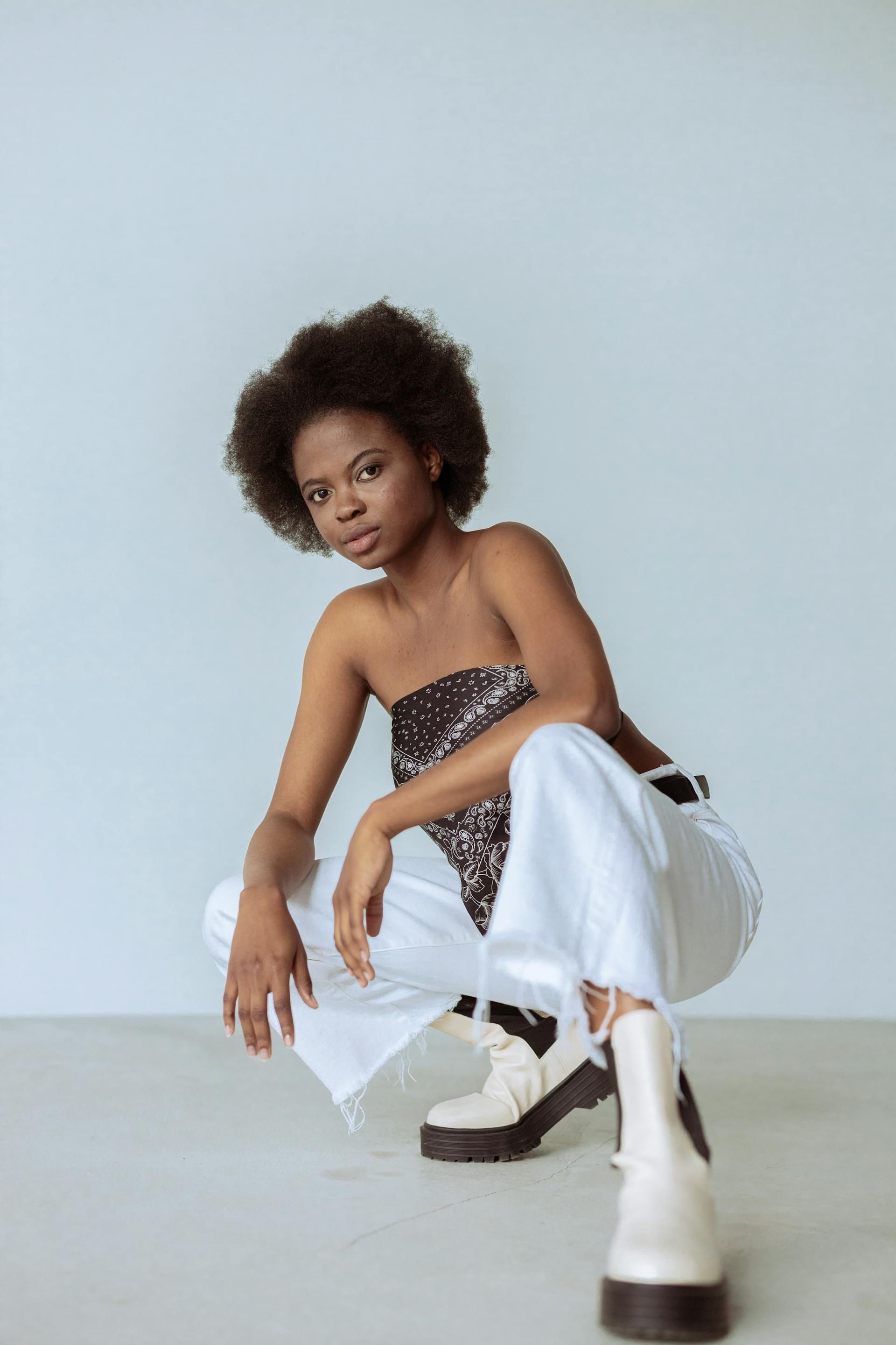 A woman is squatting down wearing white pants and white boots.