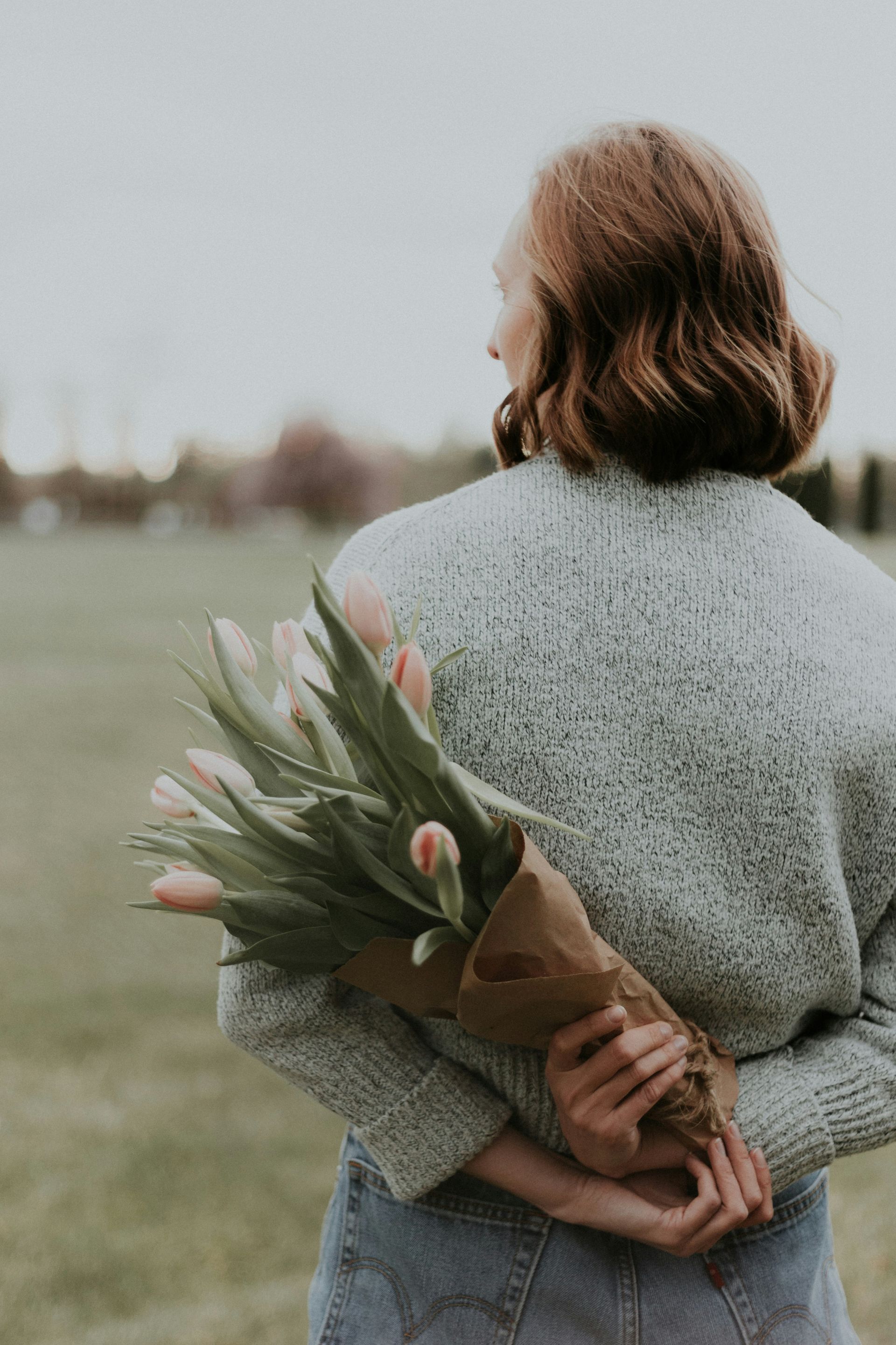 A woman is holding a bouquet of flowers behind her back.