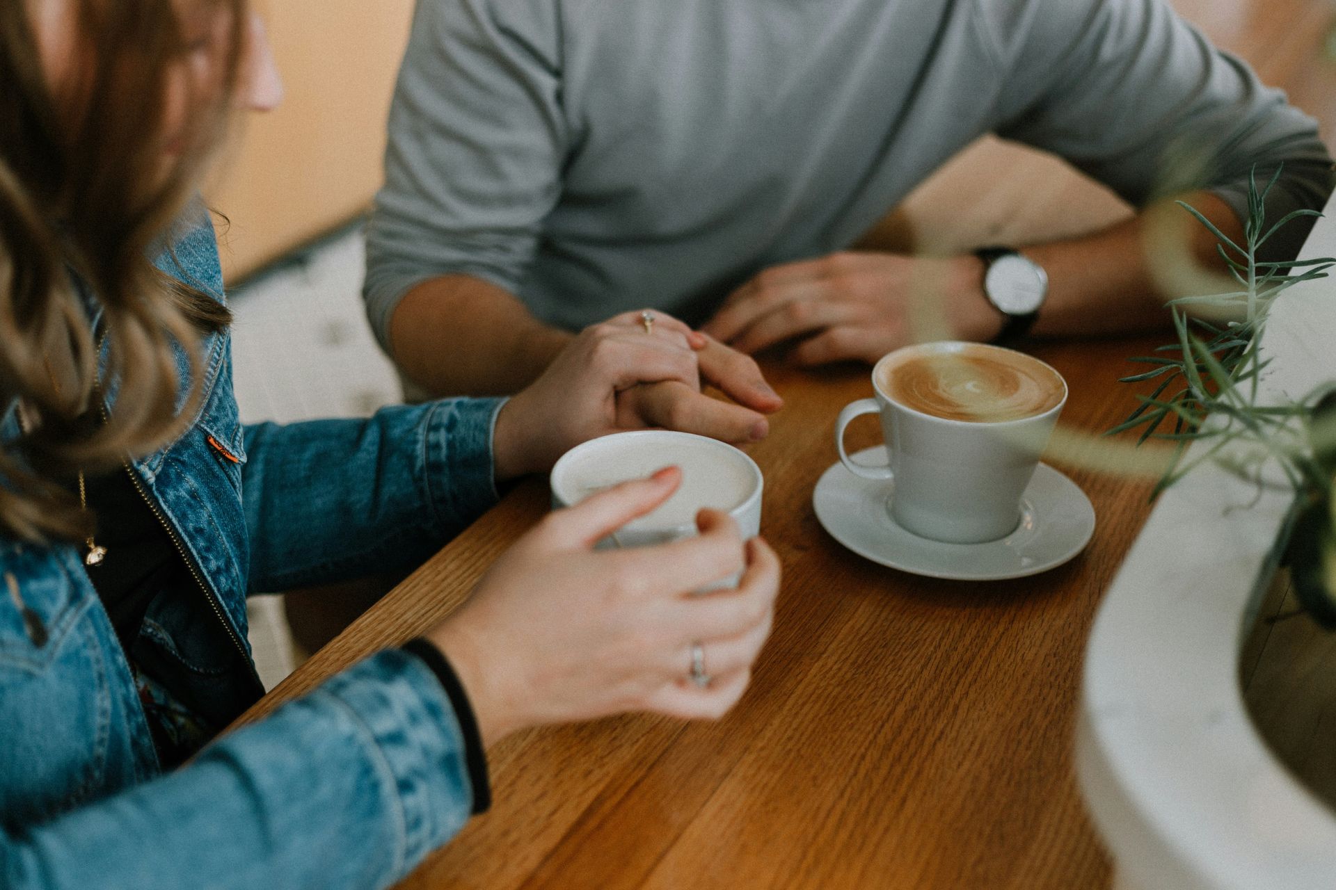 A man and a woman are sitting at a table holding hands and drinking coffee.