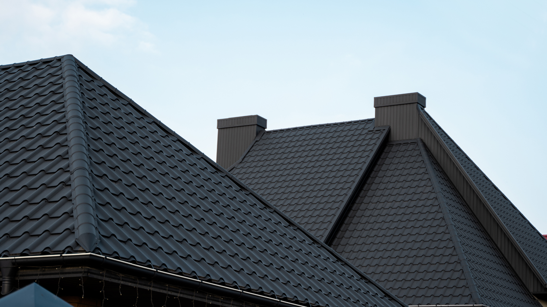 Black tiled roofs and chimneys against a light blue sky.