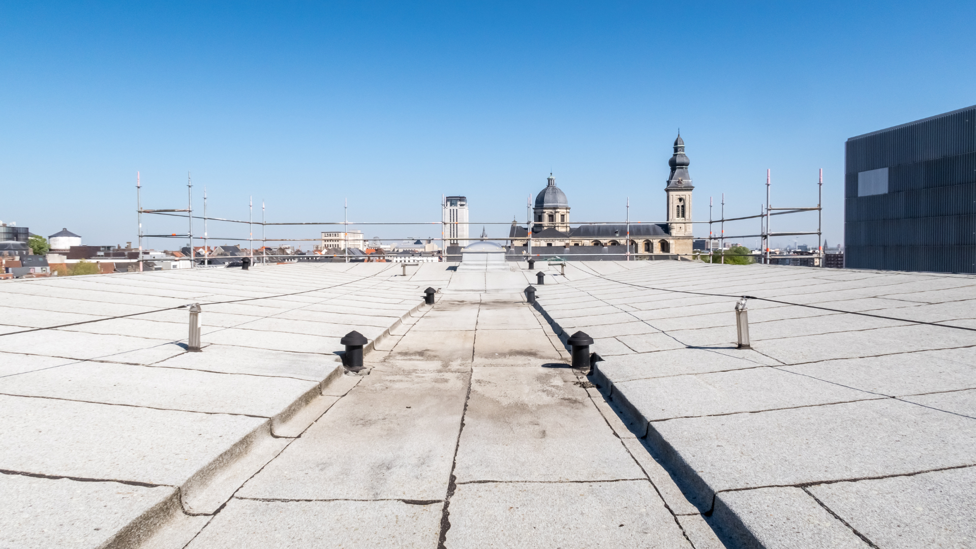Flat rooftop overlooking a cityscape with a church and clear blue sky.