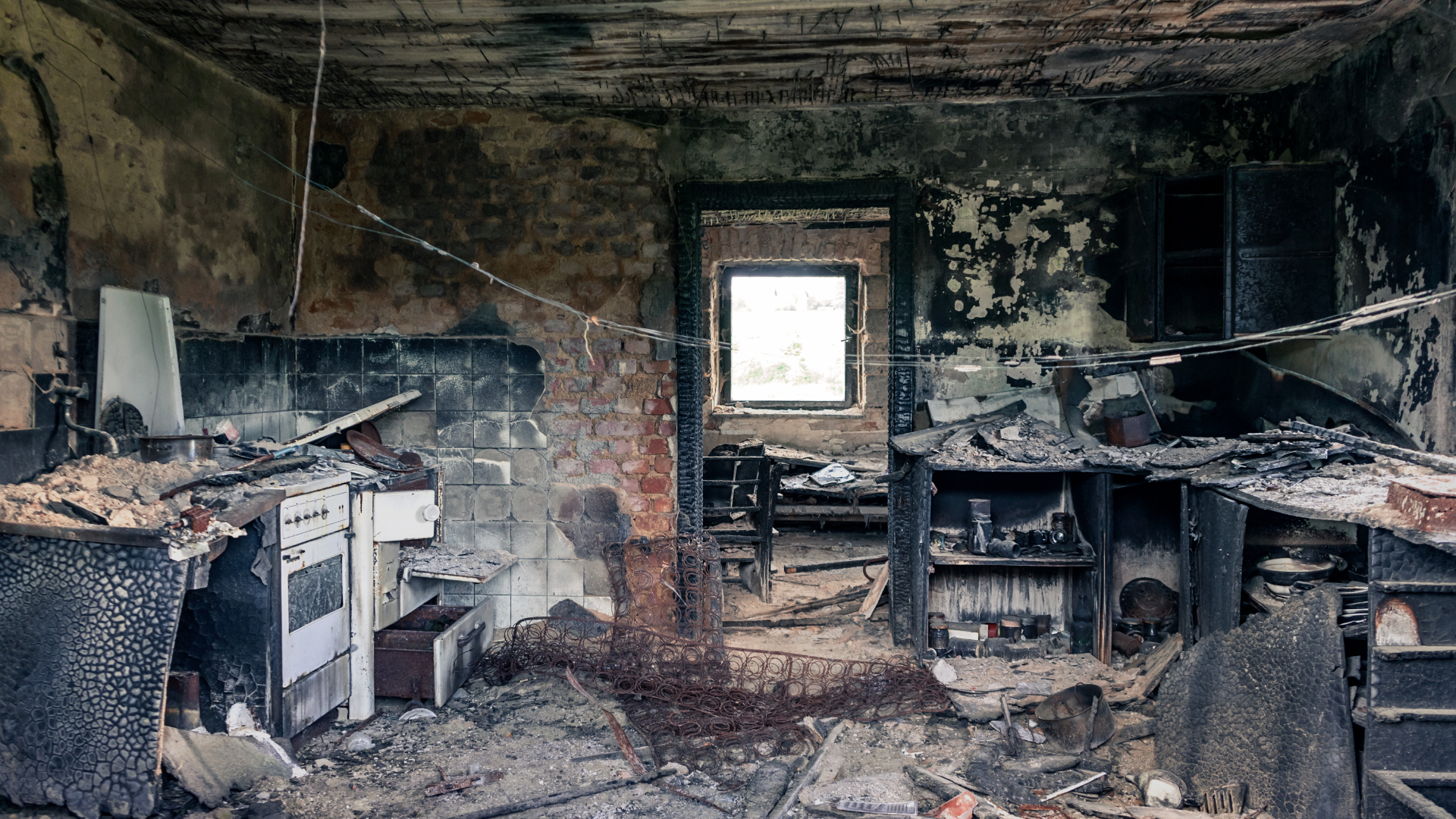Heavily damaged kitchen interior after a fire; charred walls, appliances, and debris.