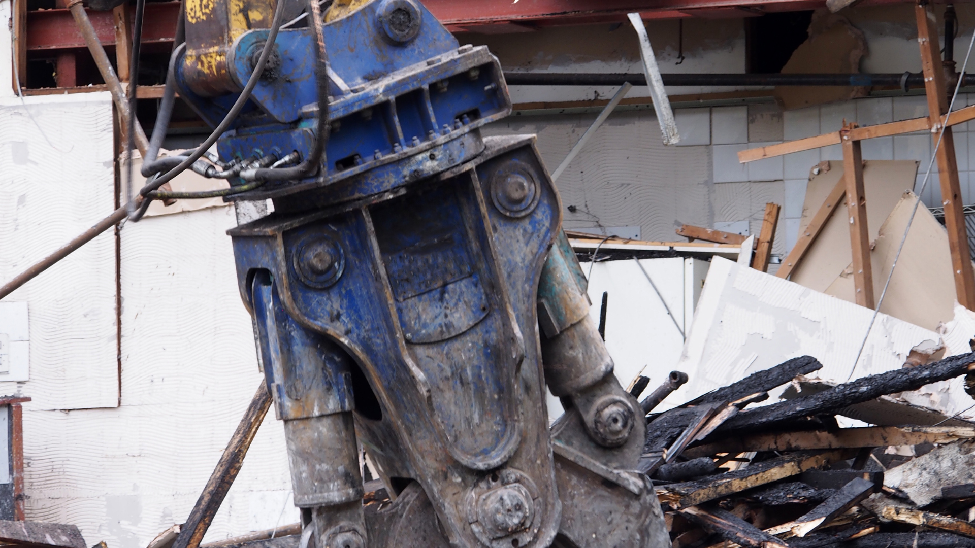 Blue demolition machine gripping and breaking apart debris and building materials.