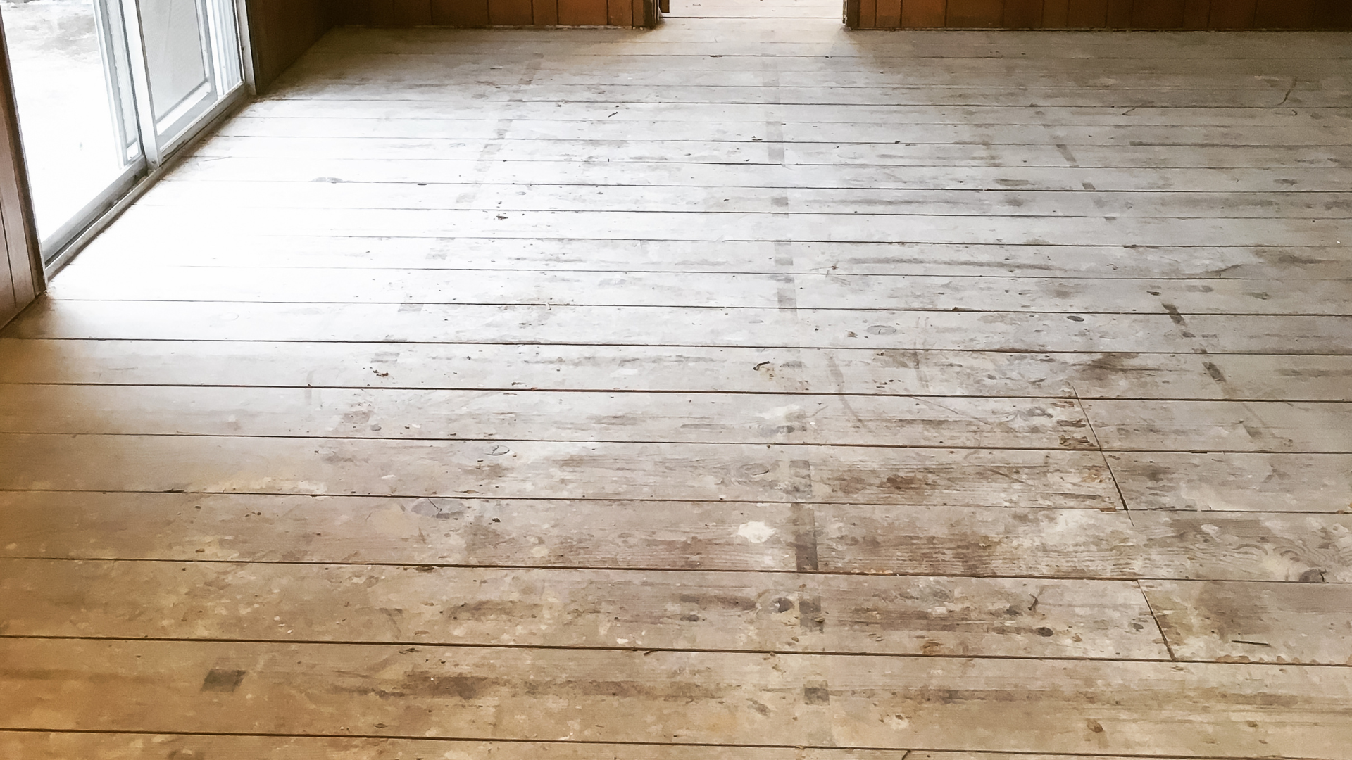 Bare wooden floorboards, worn with long, dark grooves running lengthwise, viewed from a low angle.
