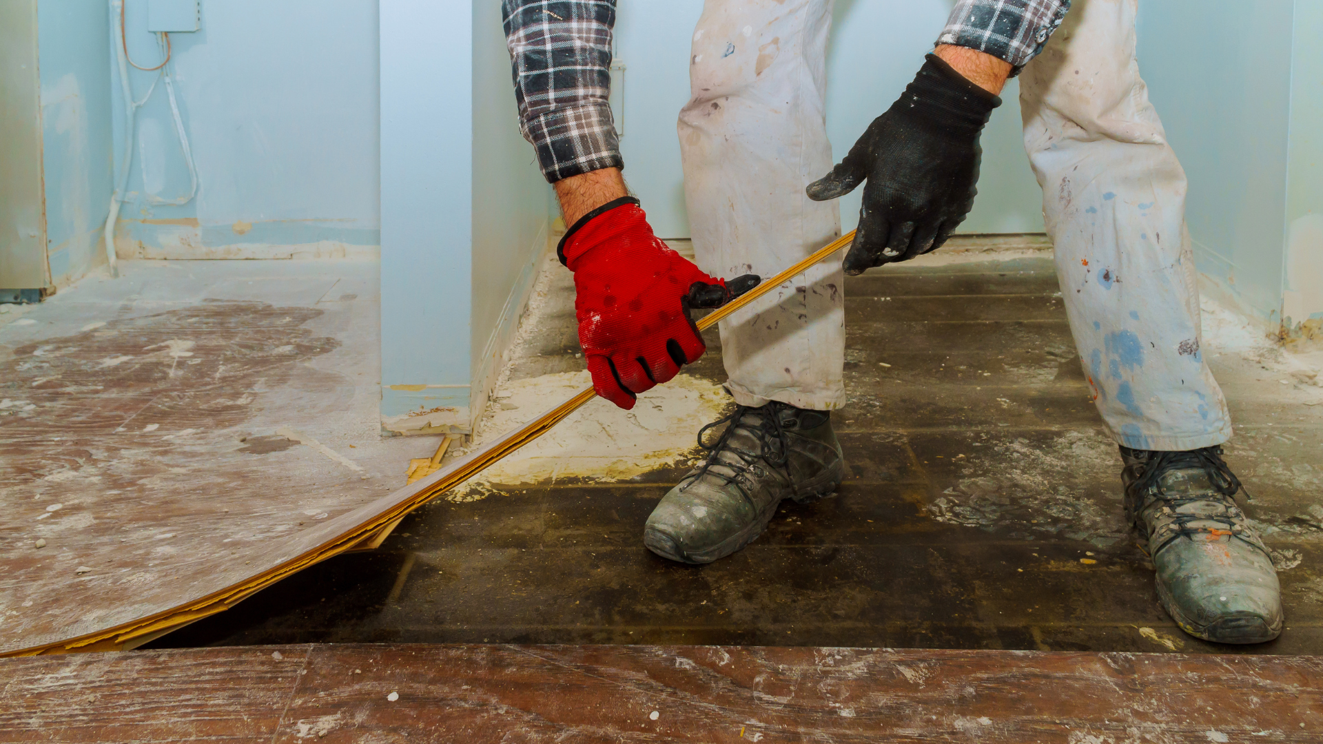 Person wearing gloves uses a tool to pry up flooring in a room.