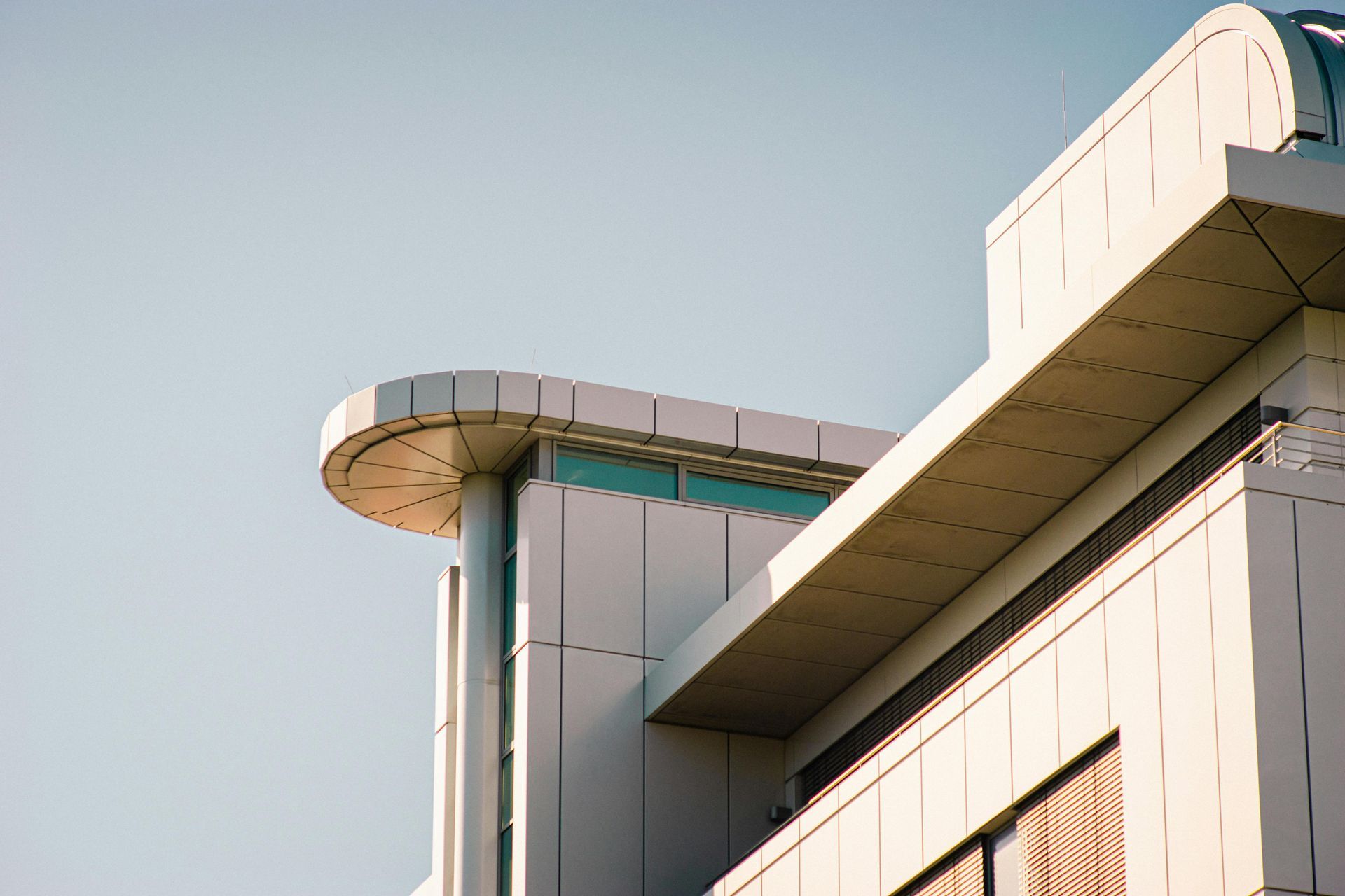 Modern building exterior with curved roof detail, white and beige panels against a clear sky.