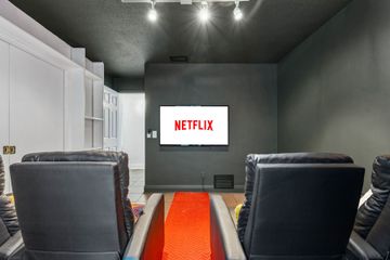 Home theater with black recliners facing a TV displaying the Netflix logo; red runner on the floor.