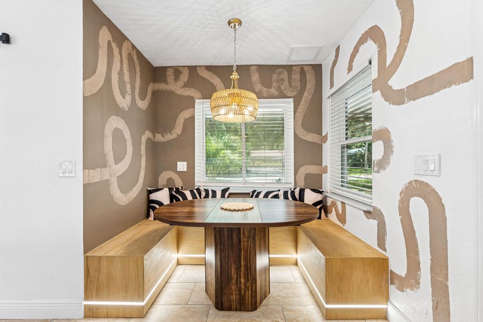 Breakfast nook with wooden table, built-in benches, patterned walls, and a decorative light fixture.