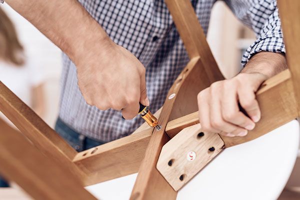 Hands using a screwdriver to assemble a wooden chair with a white seat cushion