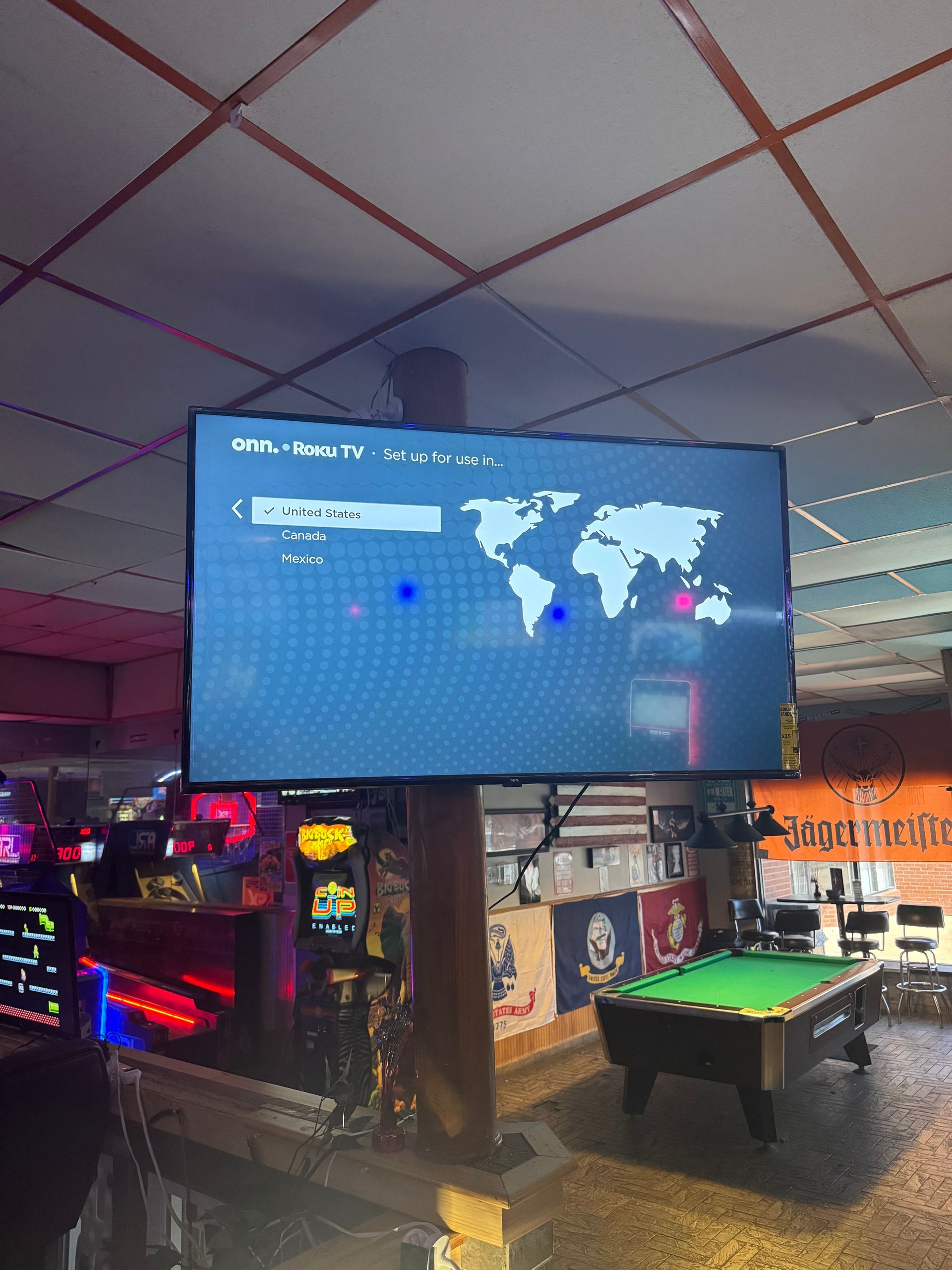 Bar screen with a large digital world map display above a pool table and colorful neon lights.