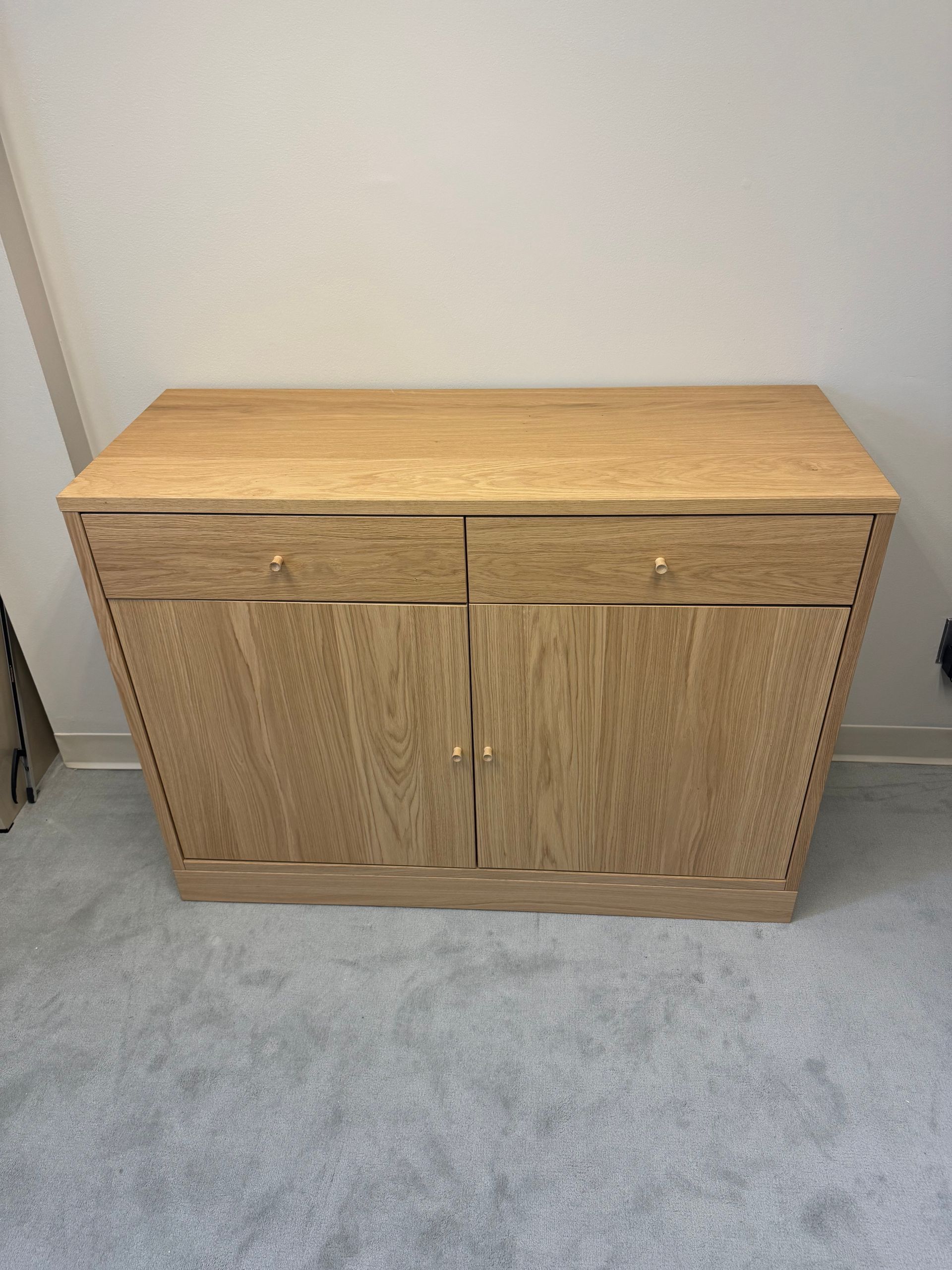 Wooden cabinet with a light wood top and two doors against a white wall on a carpeted floor