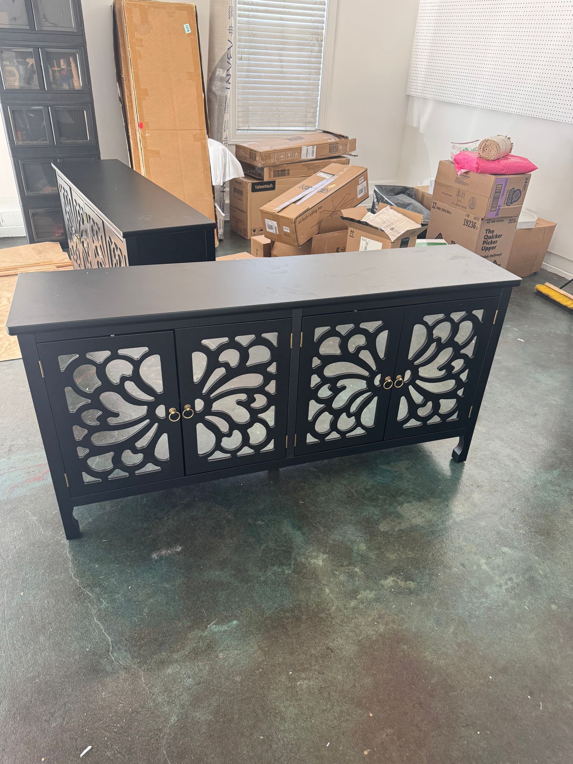 Black decorative console table with floral cutout panels in a cluttered room with boxes and furniture.