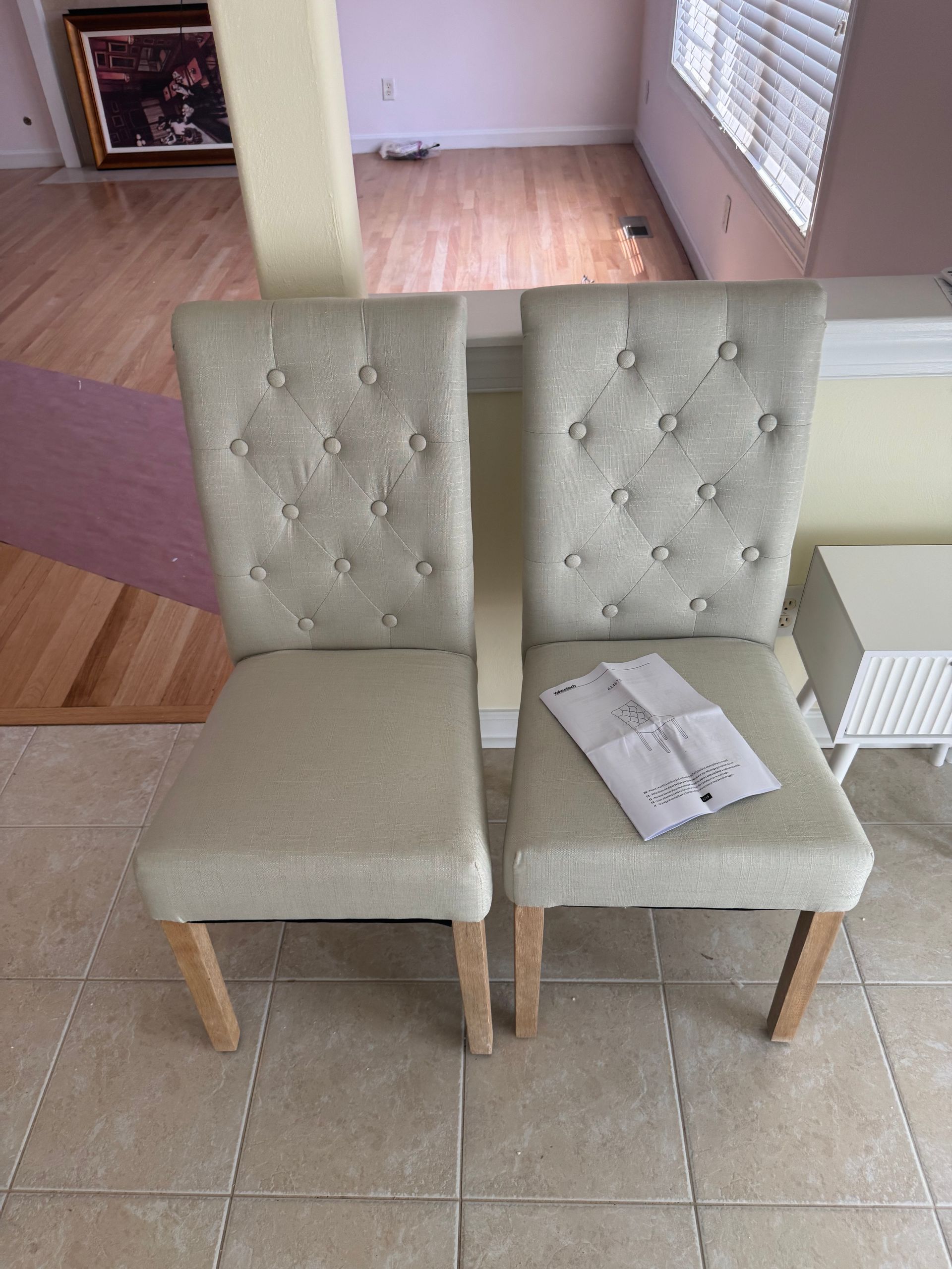 Two cream tufted dining chairs on a tiled floor, one with papers on the seat.