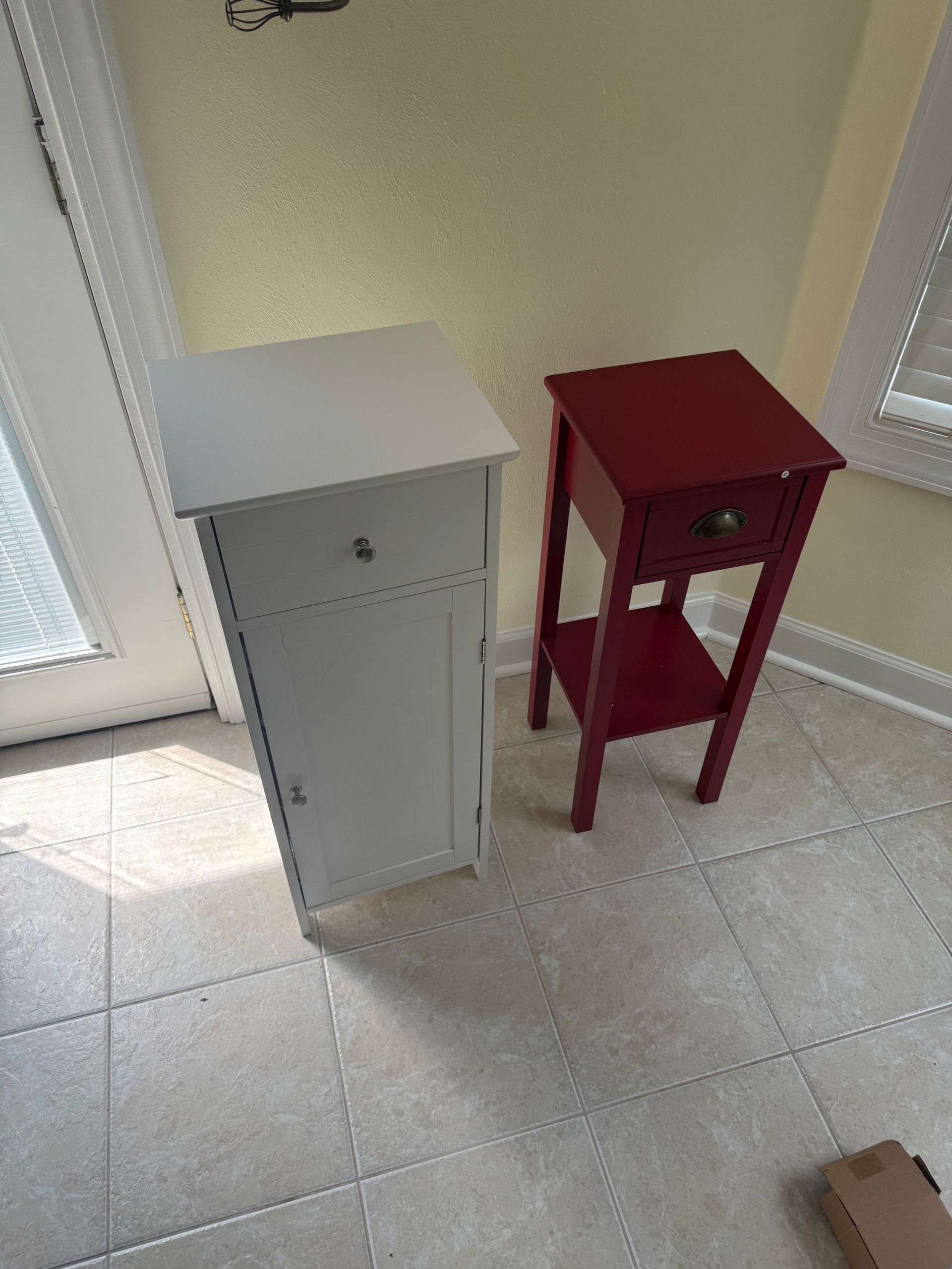 Two small side tables, one white and one red, on a tiled floor by a window.