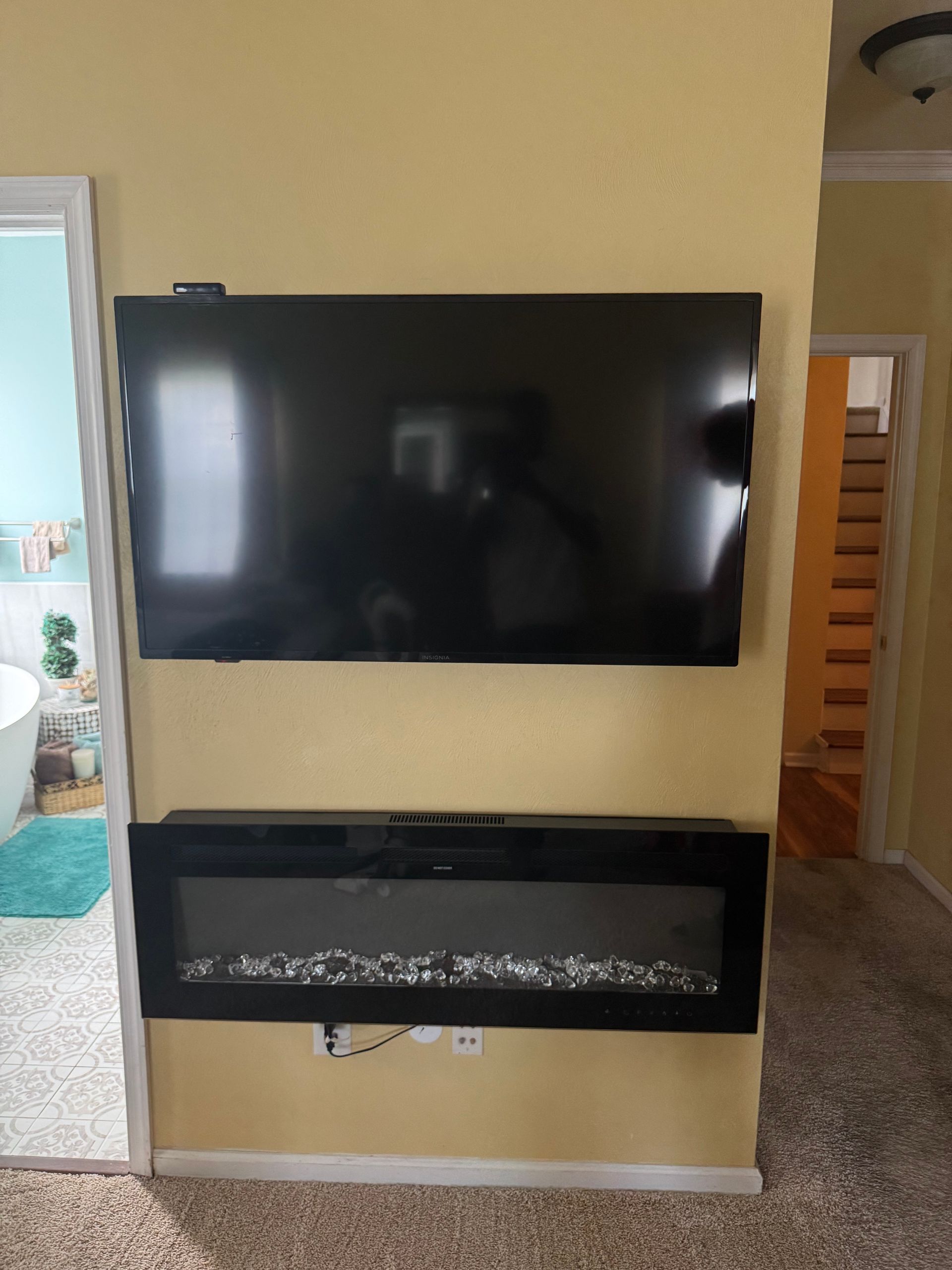 Wall-mounted TV above a black electric fireplace on a beige living room wall.