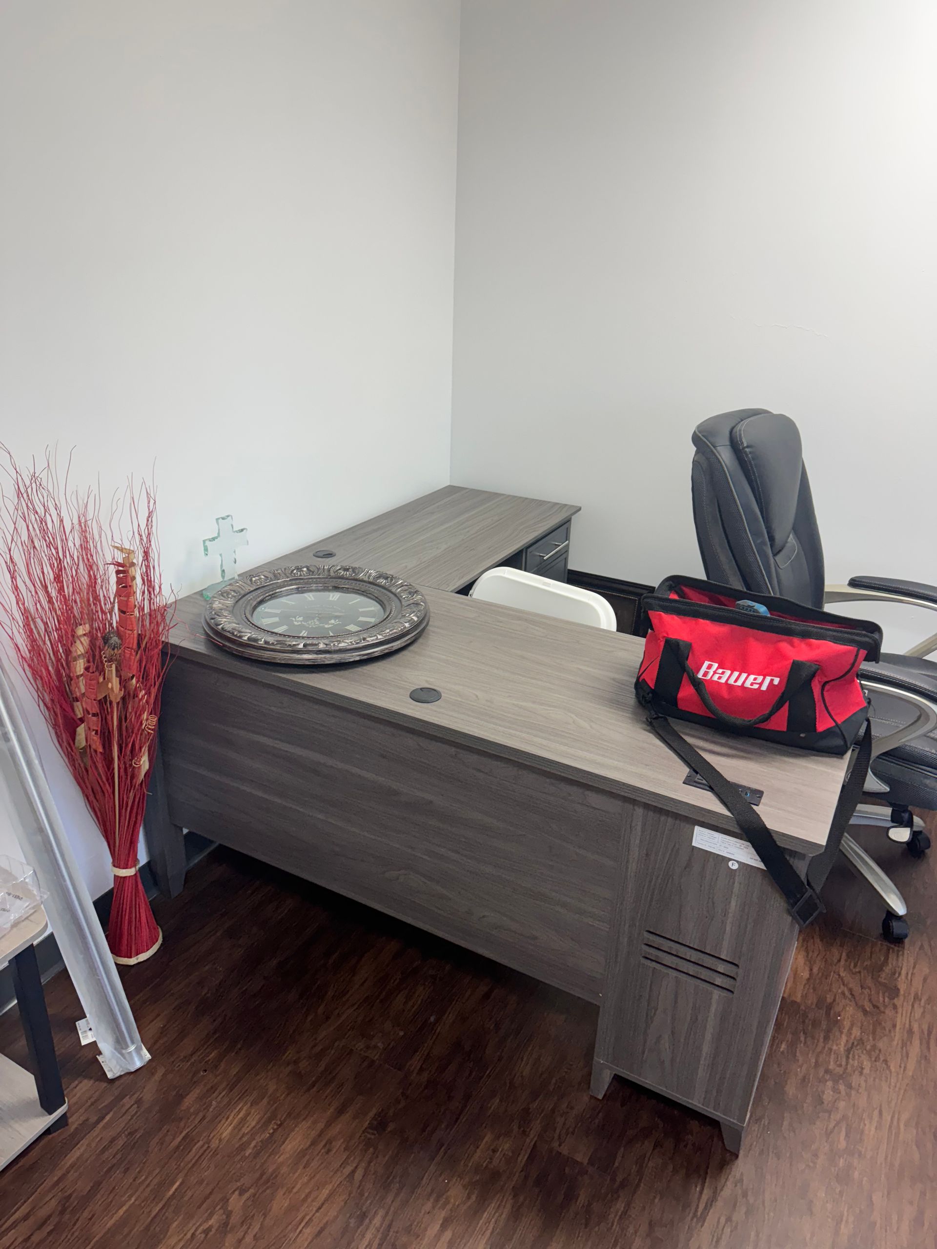 Small corner room with a low gray desk, red tool bag, tire, plate, and folded ladder on wood flooring.