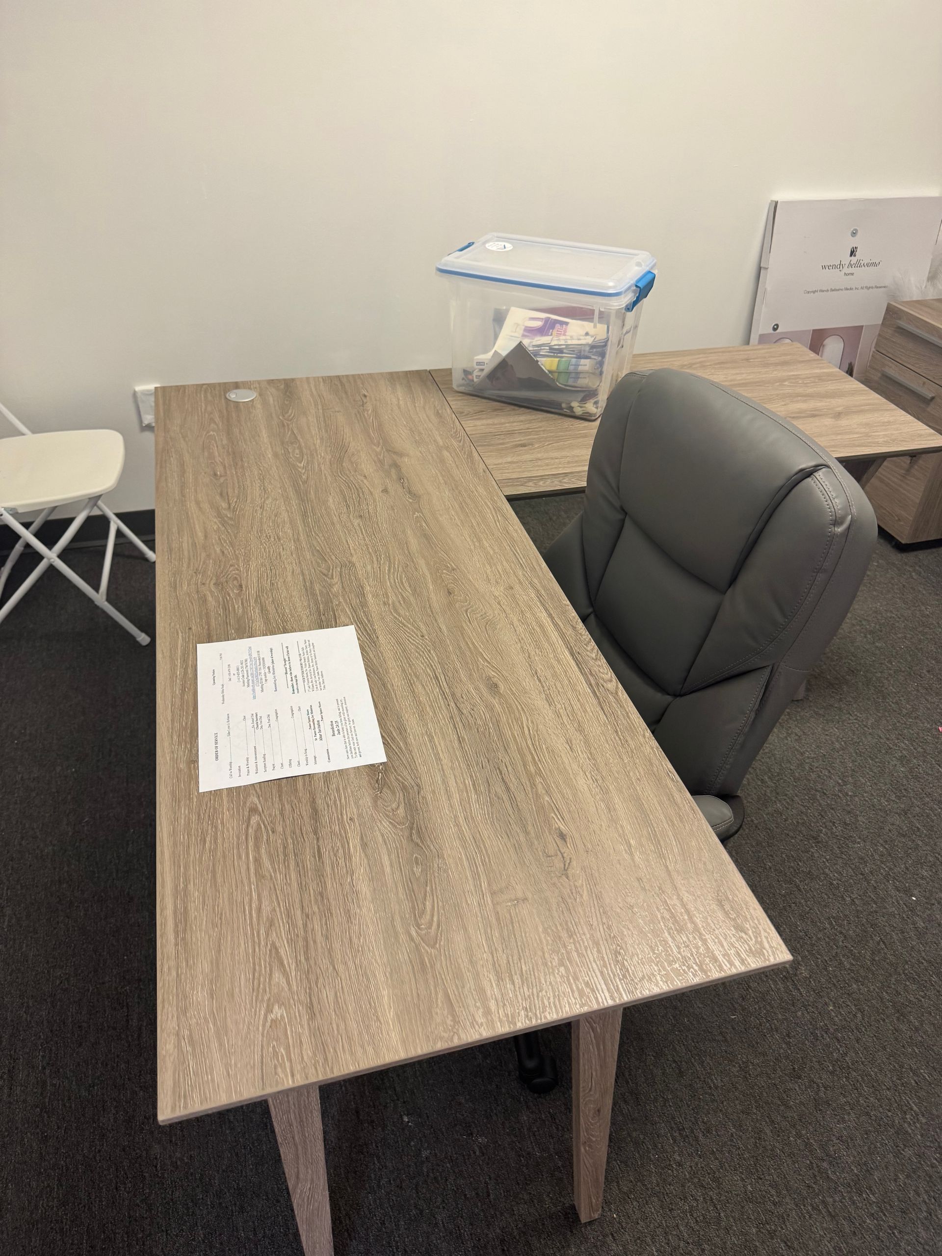 Office desk with a chair, papers, and a bag against a plain wall.