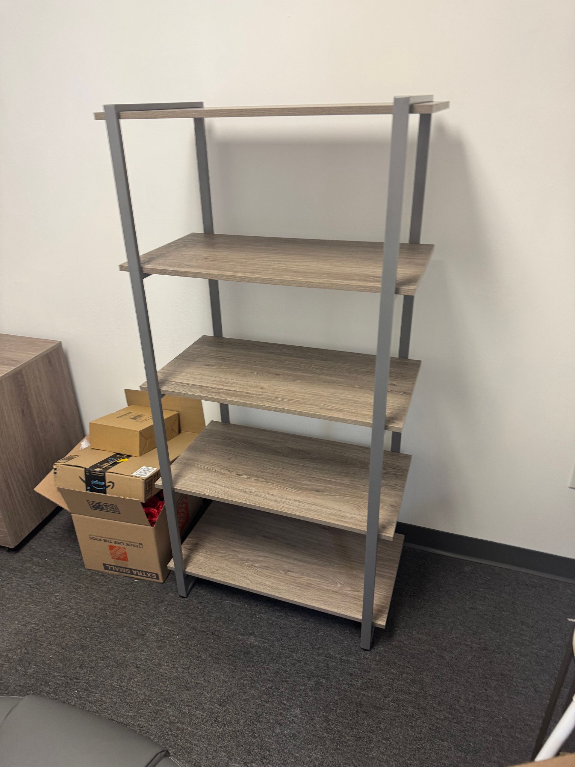 Gray metal shelving unit with three wooden shelves and cardboard boxes on a carpeted floor.