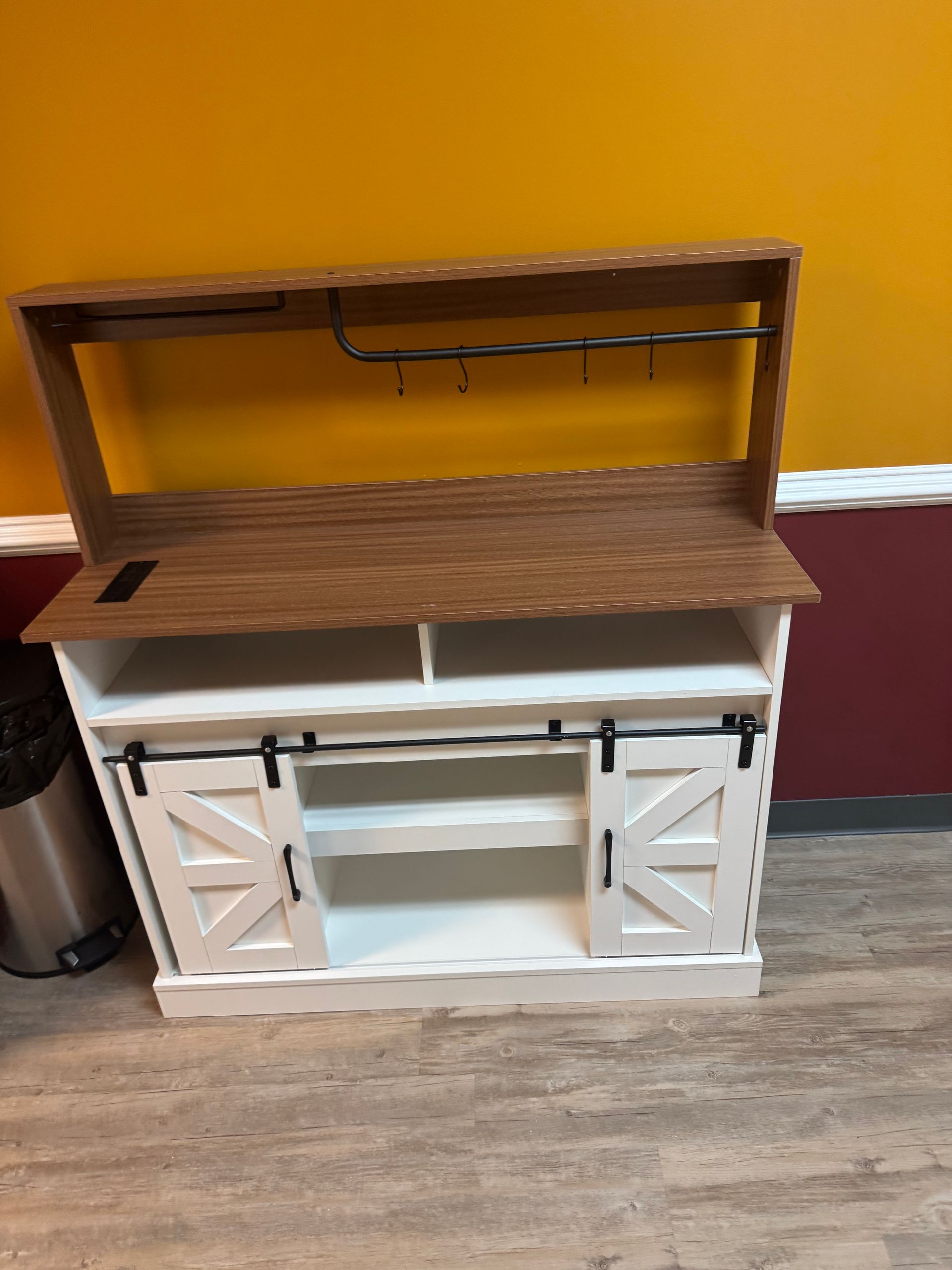 White farmhouse-style cabinet with a wood countertop and open shelf, against a mustard yellow wall.