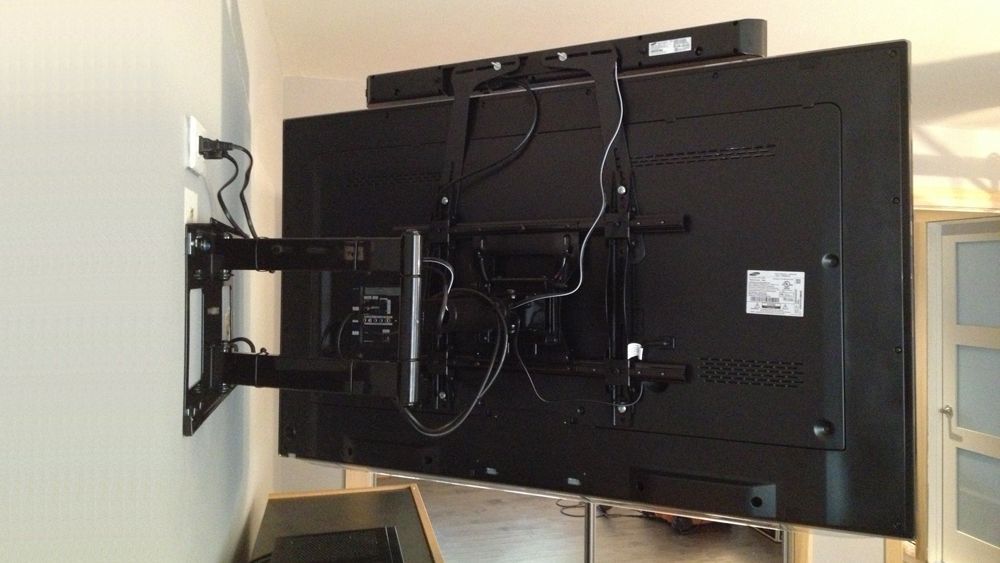 Flat-screen TV mounted on a wall bracket with visible cables and components on the back.
