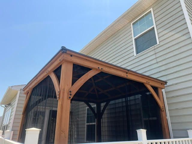 Wooden screened porch with arched supports attached to a beige house under a clear blue sky