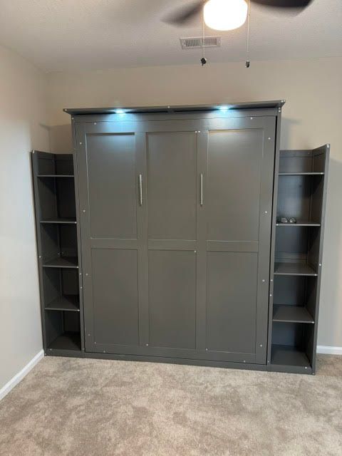 Built-in gray wardrobe cabinet with side shelves in a carpeted bedroom