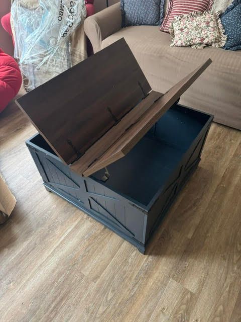 Open wooden storage chest with lid raised in a living room on a wood floor