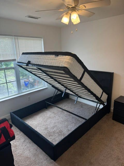 Bedroom with a black bed frame and lifted mattress, showing storage space underneath.