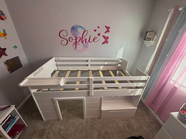 Children’s room with a white loft bed and pink “Sophie” wall decal, curtains, and carpeted floor
