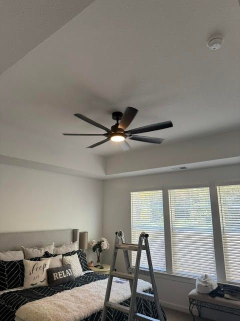 Bedroom with gray bed, ladder, ceiling fan, and large windows with blinds