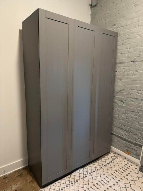 Tall gray wardrobe cabinets against a white brick wall in a room corner