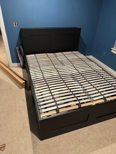 Black bed frame with slatted base in a blue bedroom, partially assembled and missing a mattress