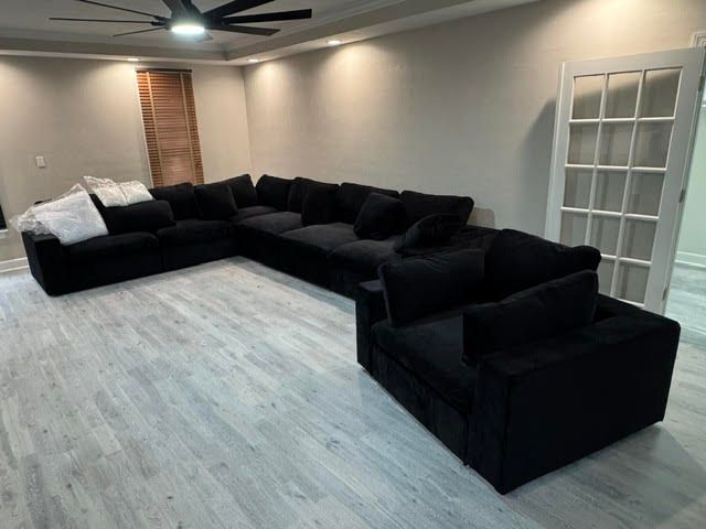 Spacious living room with black sectional sofas, light wood floor, ceiling fan, and French doors