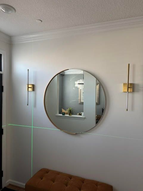 Modern living room wall with a round mirror, brass sconces, and a brown tufted bench beneath