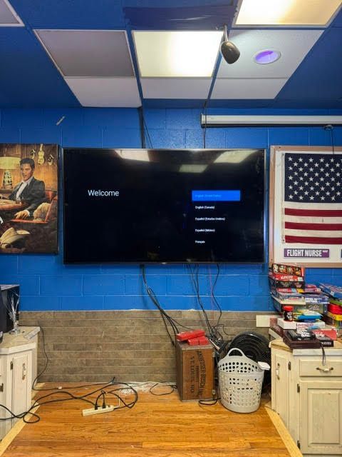 TV screen in a cluttered room with blue walls, an American flag, and shelves of supplies