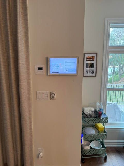 Wall-mounted control panel beside a window, with a small shelf of household items below.