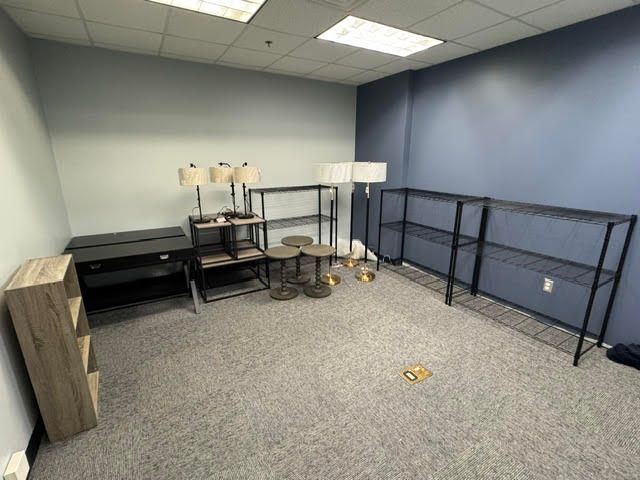 Empty office room with carpet, blue walls, desks, a TV stand, and folding table racks against the wall