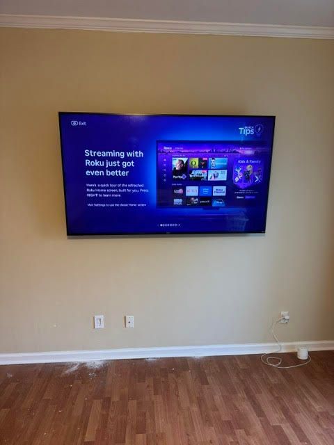 Wall-mounted TV displaying a streaming service on a beige wall above wood flooring.