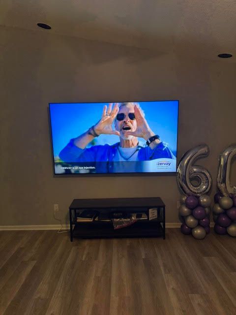 Living room with TV showing a person on a blue background, and silver “60” balloons on the right.