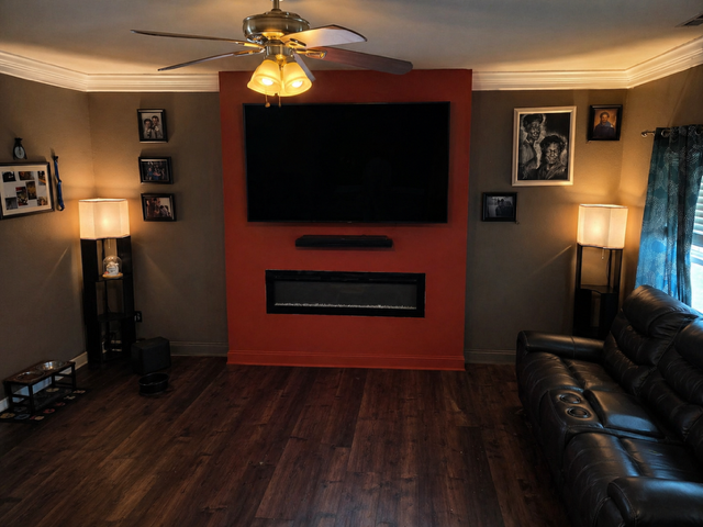Living room with wall-mounted TV, fireplace, leather sofa, and warm lamps on dark wood floors