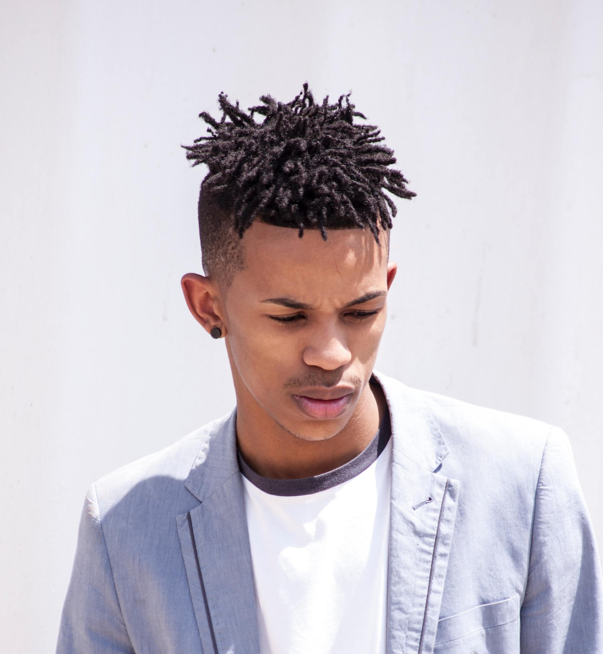 A young man with dreadlocks is wearing a grey jacket and a white shirt.