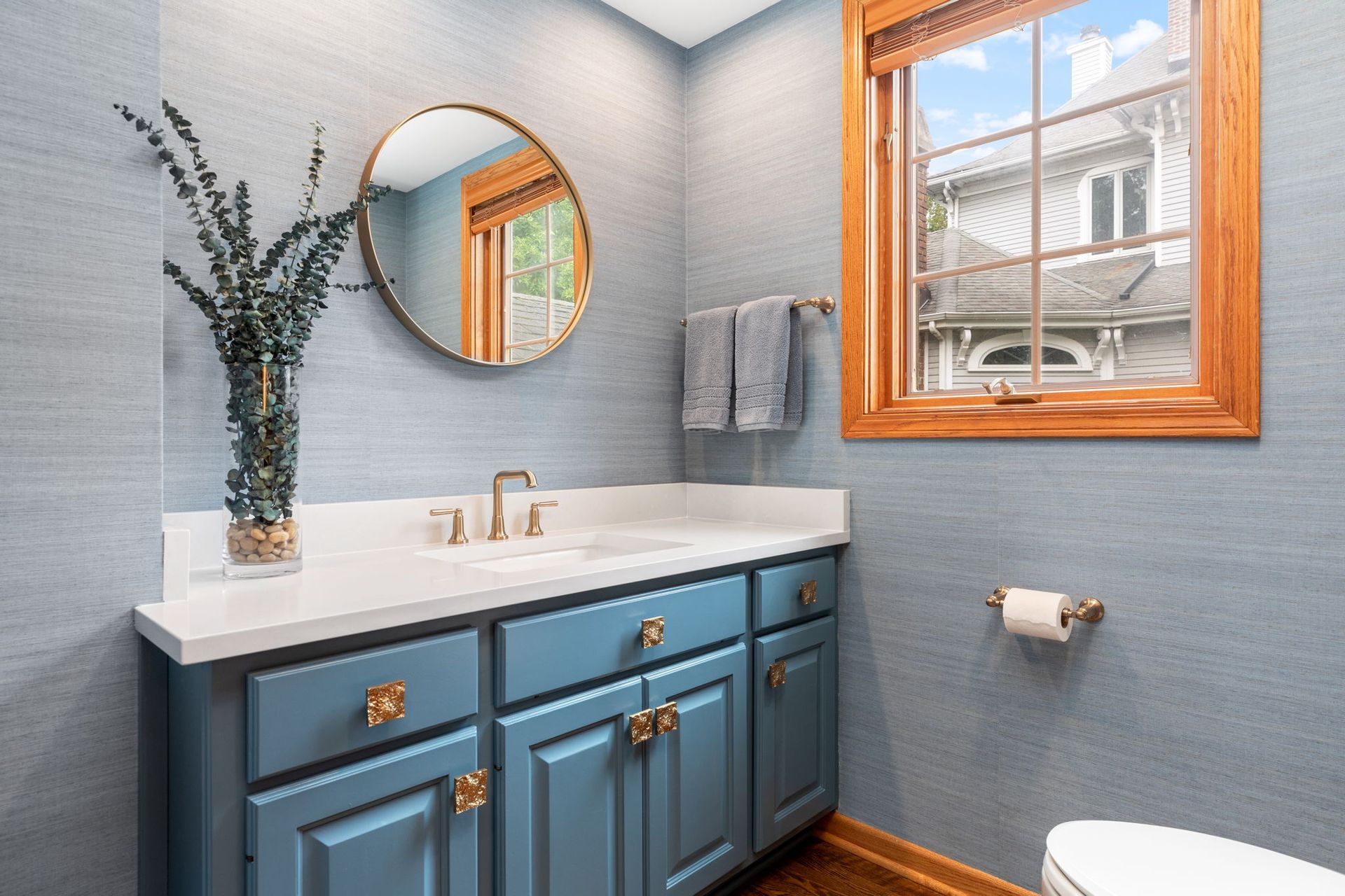 A bathroom with blue cabinets , a sink , a mirror and a window.