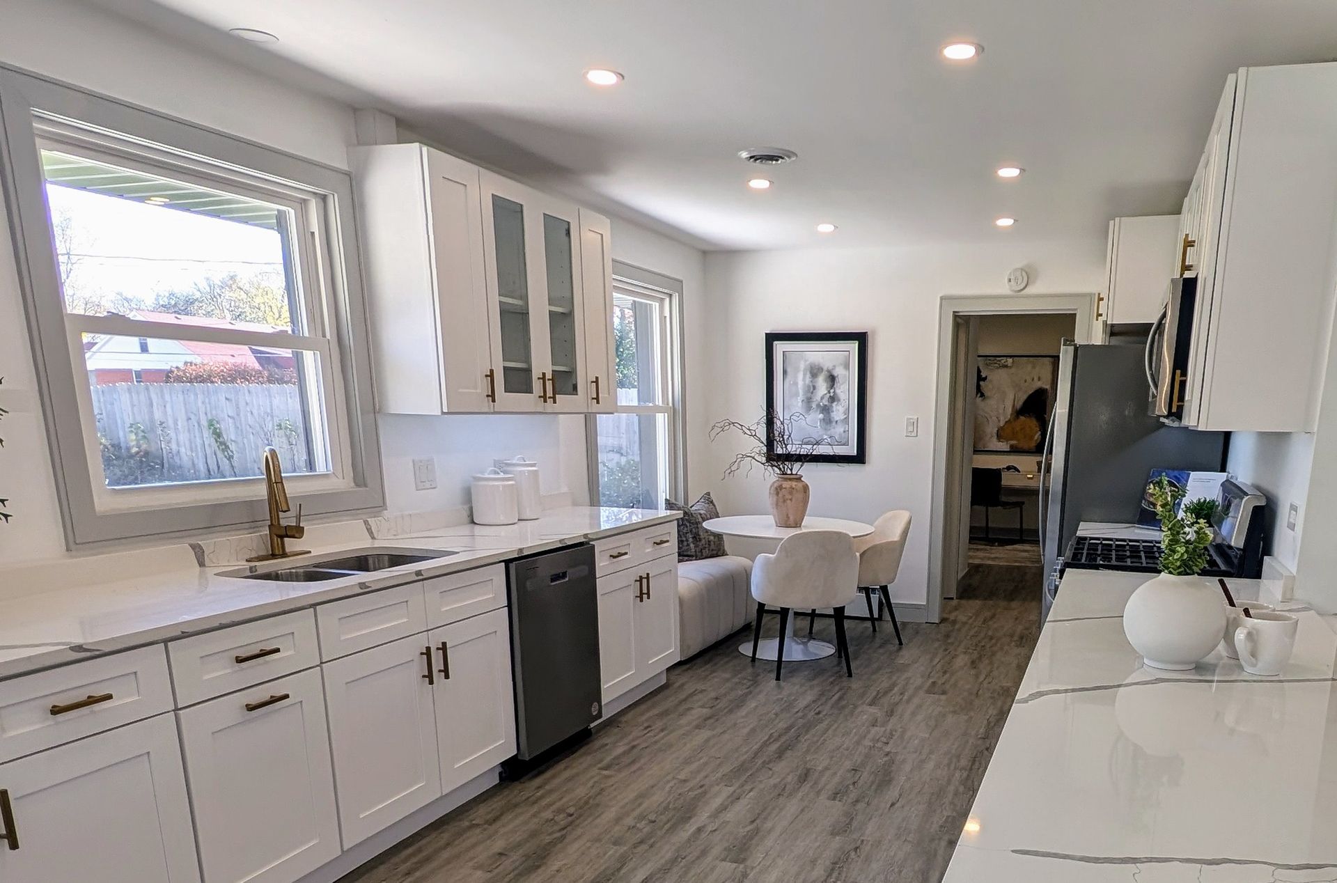 A kitchen with white cabinets , a sink , a dishwasher , a table and chairs.